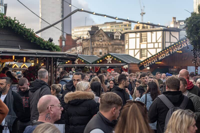 An image of a crowd at a Christmas festival with signage and lights in the back.